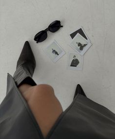 a woman's legs with black shoes and sunglasses on the floor next to photos