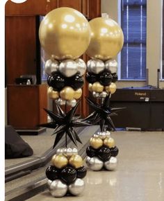 some black and gold balloons are sitting on the floor in front of a table with chairs