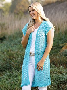 a woman standing in the grass wearing a blue crochet cardigan and white jeans