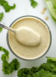 a spoon in a jar filled with dressing next to lettuce