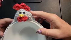 a person is holding a small crocheted chicken