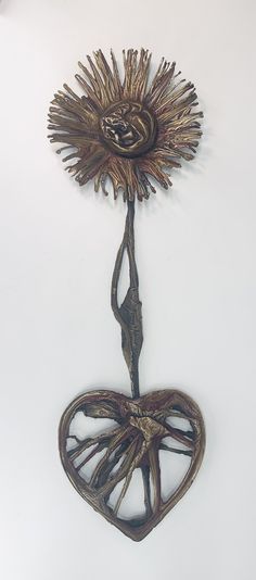 a metal sculpture with a sunflower in the shape of a heart on a white wall