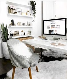 a white desk with a computer monitor on top of it next to a chair and potted plant