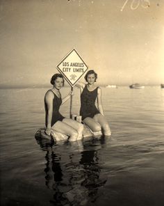 two women are standing in the water near a sign