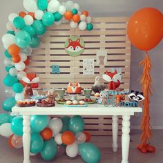 a table topped with balloons and desserts next to a wooden paneled wall filled with animals