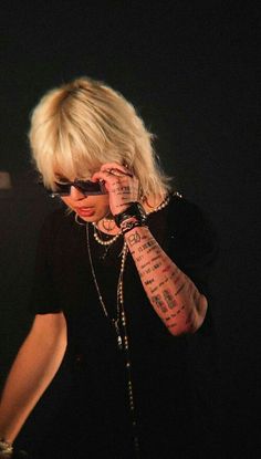 a woman with tattoos on her arm talking on a cell phone while standing in front of a microphone