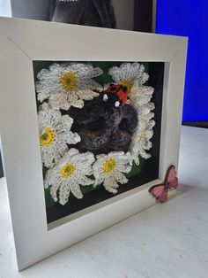 a white frame with some crocheted flowers and a small red bird in it