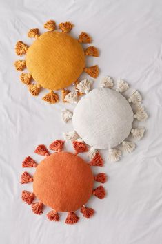 three different colored pillows with tassels on top of each one in the shape of a sun