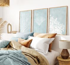 a bed with pillows and blankets on top of it next to two framed art pieces