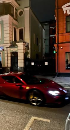 a red sports car is driving down the street in front of some buildings at night