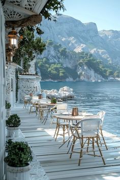 an outdoor dining area with tables and chairs on the water's edge next to mountains