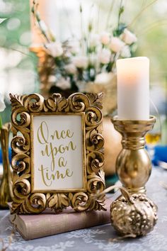 a gold frame sitting on top of a table next to a candle