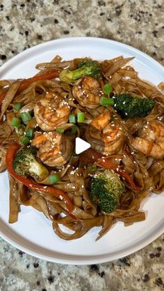 a plate with noodles, shrimp and broccoli on it sitting on a table