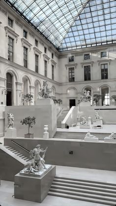 the inside of a building with statues and stairs in front of glass ceilinged skylight