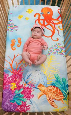 a baby laying in a crib with an octopus blanket on it's back