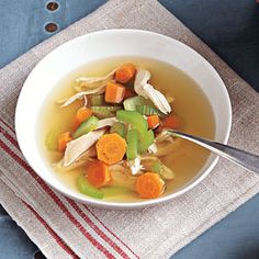 a bowl of soup with carrots, celery and chicken on a napkin