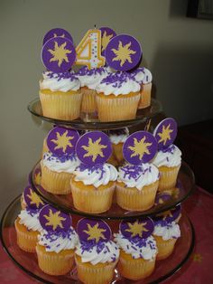 three tiered cake with cupcakes decorated in purple and yellow icing on top