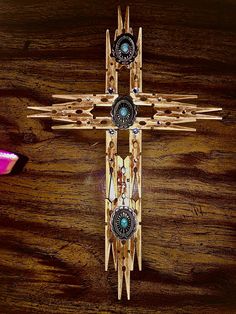 a cross made out of wooden sticks and beads on top of a wood table next to a pink flower