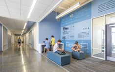 several people are sitting on benches in the hallway next to a blue wall and glass doors