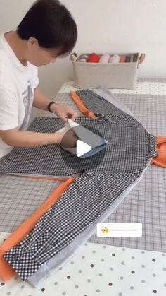 a man is cutting fabric on top of a bed with an orange and black blanket