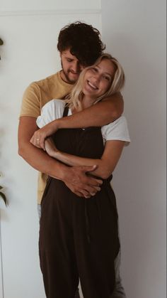 a man and woman hugging each other in front of a wall with plants on it