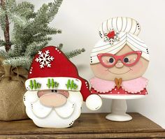 two christmas decorations on a table next to a potted plant