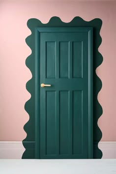 a green door with scallops on the side and pink wall in the background