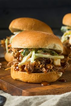 three pulled pork sandwiches with cole slaw on a cutting board