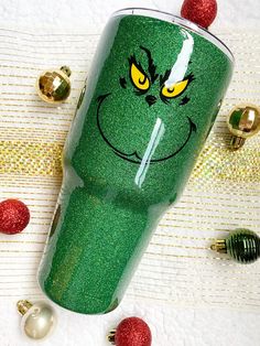 the grin face on this green tumbler has yellow eyes and is surrounded by christmas ornaments