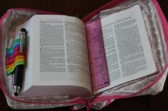 an open book sitting on top of a pink bag with a pen in the middle