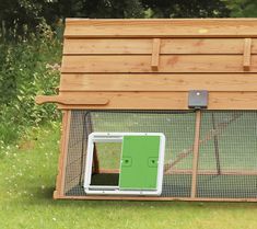 a small chicken coop with a green door and window on the outside, surrounded by grass