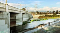 a man riding a bike down a street next to a river with power lines above it