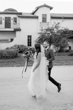 a bride and groom walking in front of a large house