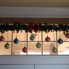 christmas ornaments hanging from the window sill in front of an open door with green and red baubes