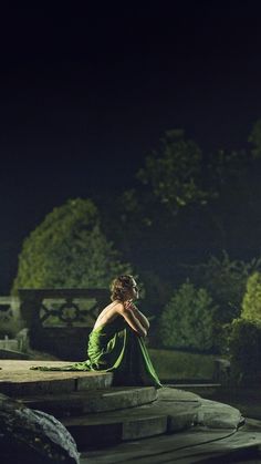 a woman in a green dress sitting on steps at night with her back to the camera