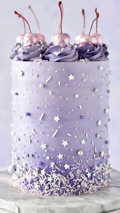 a purple cake with sprinkles and cherries on top