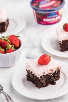 three pieces of chocolate cake on white plates with strawberries and yogurt in the background