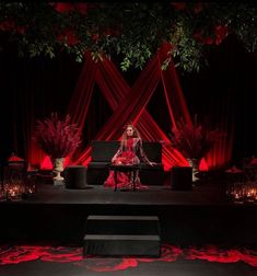 a woman sitting on top of a black couch in front of a red stage curtain