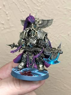 a person holding up a miniature warhammer with purple hair and blue paint on it