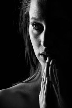 black and white photograph of a woman with her hands clasped to her chest, in front of a dark background