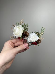 two white roses and pine cones are being held by someone's hand