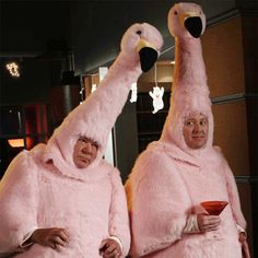 two women dressed in pink flamingos and holding cups with their arms up to the side