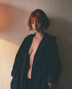 a woman with red hair and no shirt standing next to a wall in front of a lamp