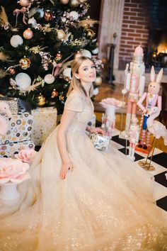 a woman sitting in front of a christmas tree wearing a dress and holding a present