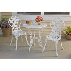 an outdoor table and two chairs with flowers on the side walk next to a window