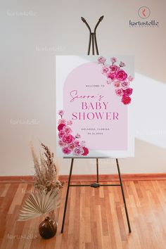 a baby shower sign sitting on top of a wooden floor next to a vase with flowers