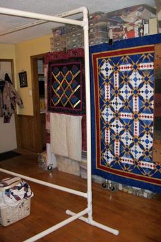 two quilts are hanging on the wall in a room with wood floors and white pipes