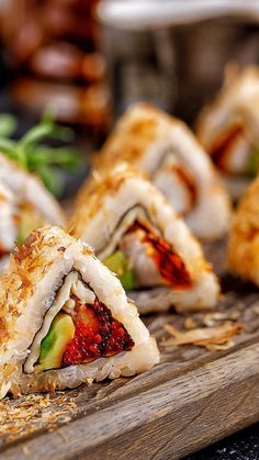 several sushi rolls are arranged on a wooden cutting board with other food items in the background