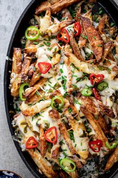 a skillet filled with cheesy french fries covered in cheese and peppers