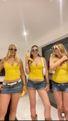 three beautiful young women in short shorts and yellow shirts standing next to each other holding bananas